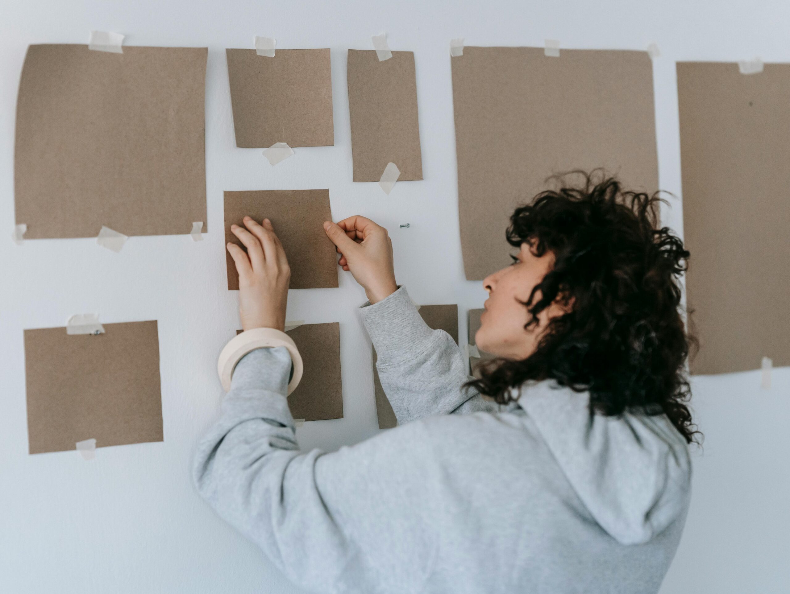 Woman using paper templates and painter’s tape to plan a gallery wall layout, a smart and easy method for hanging wall art with proper spacing and alignment.
