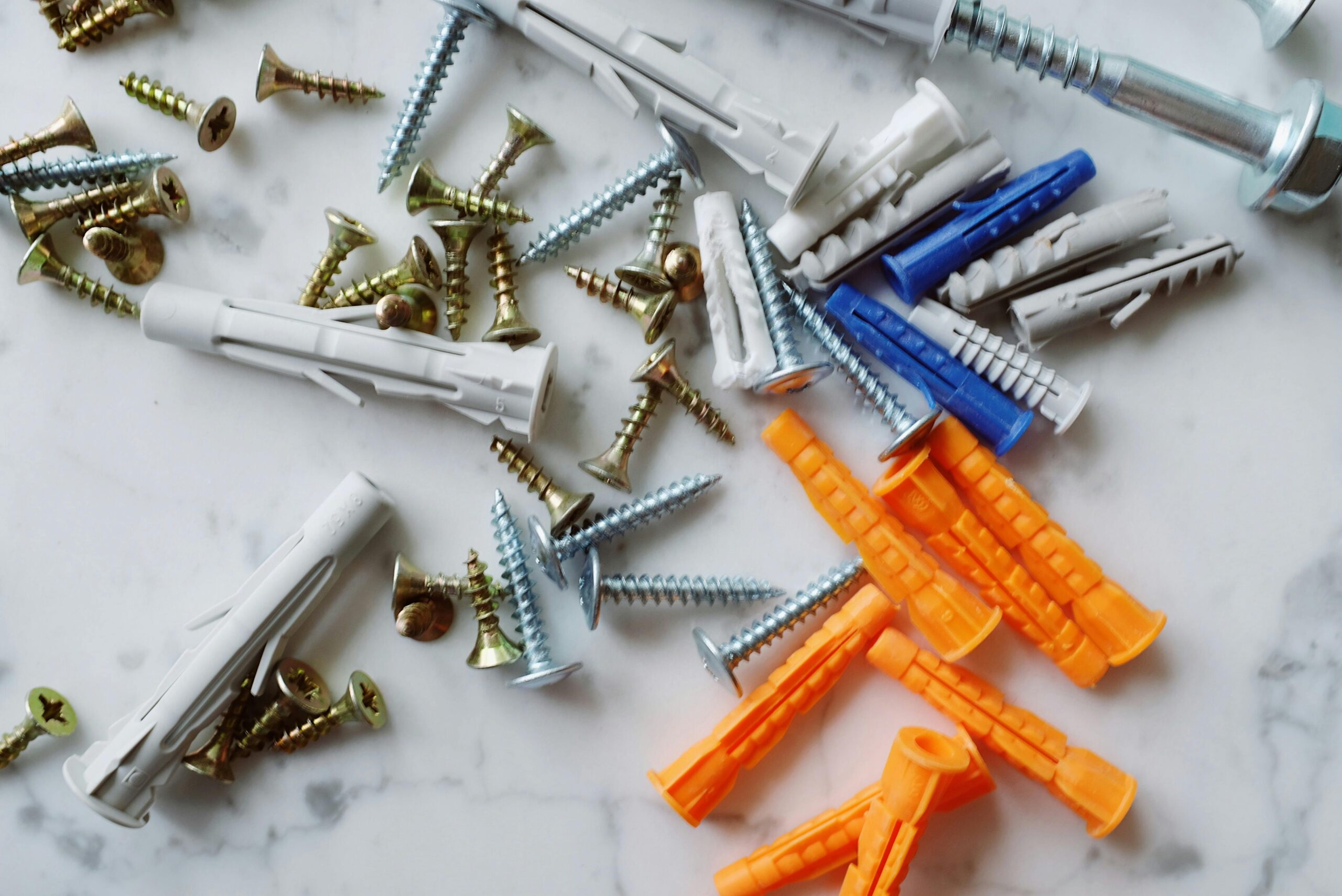 Wall anchors and screws in assorted sizes and colors on a marble surface, used for securely hanging wall art on drywall, plaster, or masonry walls.